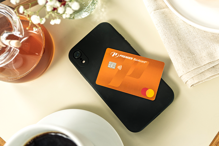 orange PREMIER bankcard credit card sitting on top of phone on a table