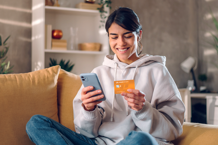 woman sittihng on couch looking at phone and credit card