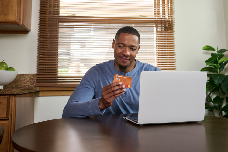 man in blue shirt sitting at a table with a laptop, looking at an orange PREMIER credit card