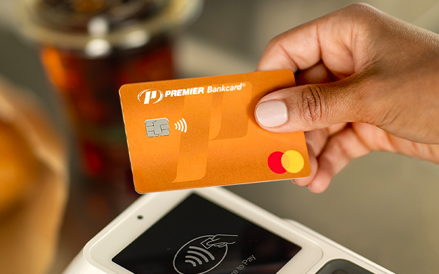 hand holding an orange PREMIER Bankcard Mastercard over a credit card machine