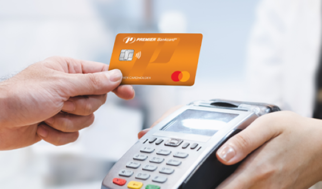 A hand holding an orange credit card next to a credit card machine